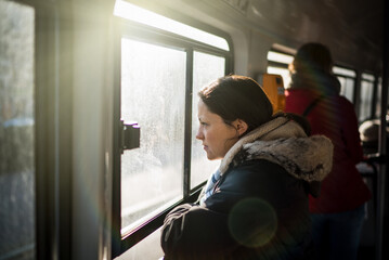 Woman tourist traveling on a tram sunny summer day happy smiling and looking out of train window whilst commuting through city with other passengers and bright sun rays