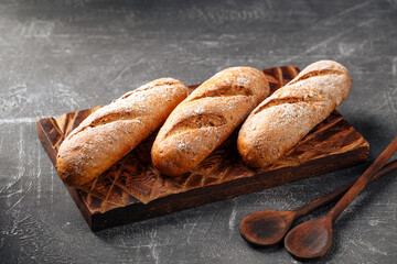 Three loafs of fresh baked baguette on the wooden cutting board on gray background