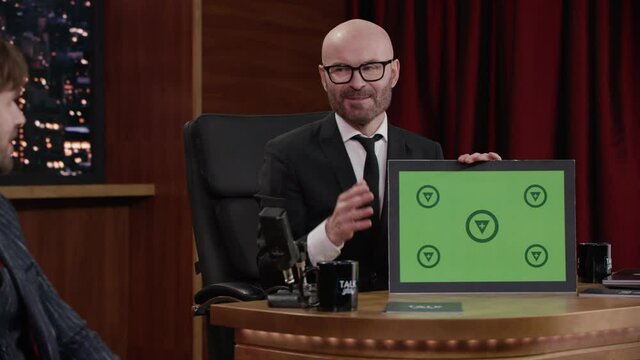 FIXED Late-night talk show host showing a green board with tracking points to celebrity guest in a studio. TV broadcast style show. Shot with RED cinema camera