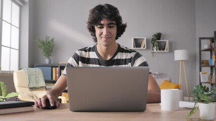 young man sits at his desk opens laptop and start working zoom out motion,arab middle eastern male student opening and using computer from home in modern living room - Powered by Adobe