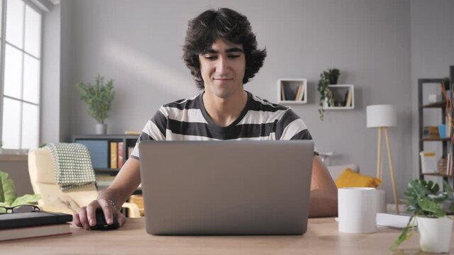 young man sits at his desk opens laptop and start working zoom out motion,arab middle eastern male student opening and using computer from home in modern living room
