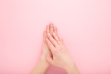 Mature woman hands on light pink table background. Pastel color. Closeup. Point of view shot. Care about clean, beautiful, soft hands skin and nails in old ages. Top down view.