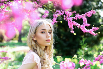 Obraz na płótnie Canvas Spring bloom concept. Beautiful female face with perfect skin. Girl on dreamy face, tender blonde near violet flowers of judas tree, nature background. Beautiful Young Spring Woman.