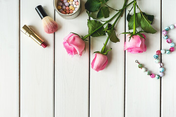 Top view arrangement with make-up, roses, necklace and copy-space on white wooden background