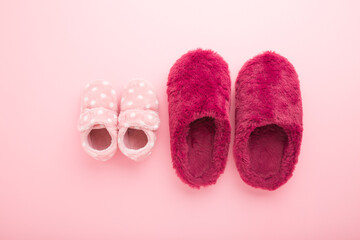 Beautiful soft warm mother and baby girl slippers on light pink table background. Pastel color....