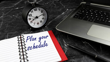 A word Plan Your Time on notebook with clock and laptop on black marble surface. Concept for time management and business. 