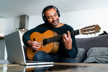 Relaxed man playing the guitar at home and using a laptop