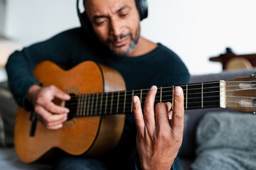 Black man playing the guitar at home and using a laptop
