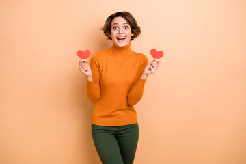 Photo of young beautiful smiling excited crazy amazed girl holding two little paper hearts isolated on beige color background