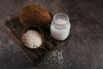 Coconut, flakes and coconut oil in jar on dark background. Healthy cooking concept