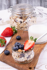 Healthy breakfast with homemade yoghurt and fresh strawberries and blueberries, muesli, milk on a white wooden table in rustic style, close up, vertical.