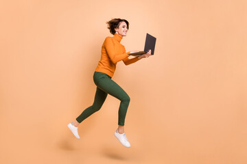 Fototapeta na wymiar Full length photo of funky sweet girl orange turtleneck communicating modern gadget jumping isolated beige color background