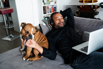 40 years old man relaxing on the sofa and watching a movie next to his bulldog