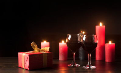 Burning candles in the dark on a wooden table. Glasses of red wine. Gift in a red package and a gold bow. St. Valentine's Day. Love