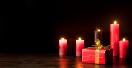 Burning candles in the dark on a wooden table. Gift in a red package and a gold bow. St. Valentine's Day. Love