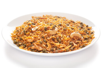 Hot spicy Kashmiri Mixture (Namkeen) snacks in a white ceramic plate made with dry fruits, peanuts, corn flakes, etc. Pile of Indian spicy snacks, under backlight, side view