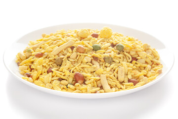 Delicious Khatta Meetha in a white ceramic plate, made with peanuts, sugar, raisins, and besan sev. Pile of Indian spicy snacks (Namkeen), under backlight, side view
