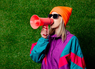 Style girl in 80s sportsuit with megaphone on green grass background