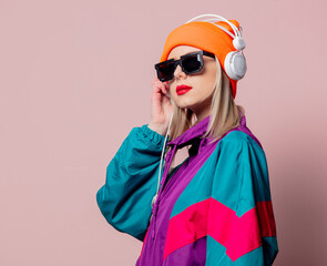 Style girl in 80s sportsuit and sunglasses with headphones on pink background