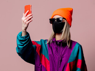 Style girl in 80s sportsuit and face mask using mobile phone on pink background