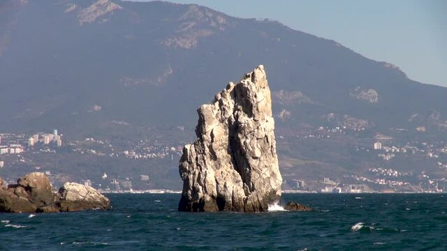 Black Sea waves of emerald color are broken on Sail rock. Southern coast of Crimea. Rock Sail grew out of depths of ea against backdrop of Crimean mountains stretching into water. 