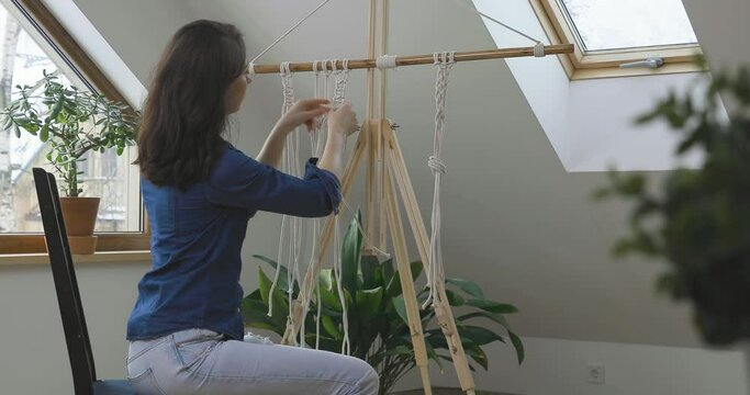Woman relaxing and making macrame at home with different knots on a sunny day at home in attic. Stay at home hobbies.	