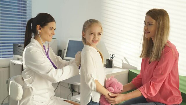 Girl visiting doctor.female pediatrician checking little patient's lungs, listening to girl's breath through stethoscope during check-up at clinic or hospital.