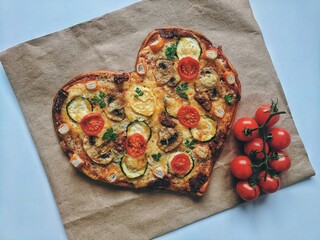 Delicious vegetarian heart shaped pizza with tomatoes, vegetables and cheese for Valentine's Day on blue background. Creative food concept of romantic love. Top view, flat lay.