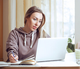 Young woman using laptop, communicates on internet with customer at home