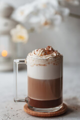 Hot latte macchiato with delicious foam in a tall transparent glass on an easy table setting. Photo in a high key. Breakfast time. Rustic background.