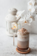Hot latte macchiato with delicious foam in a tall transparent glass on an easy table setting. Photo in a high key. Breakfast time. Rustic background.