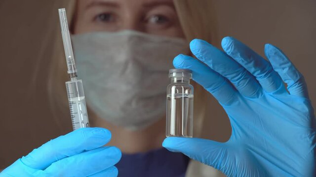 Portrait woman doctor in white hazmat protection holding vaccine ampoule in hand close-up. Coronavirus vaccination. New medication. Health care concept.