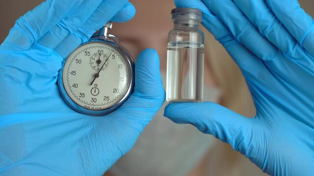 Portrait of female doctor in protective suit with an ampoule of vaccine in his hand and stopwatch close-up. new medicine. concept of development and timing of vaccination of world's population.