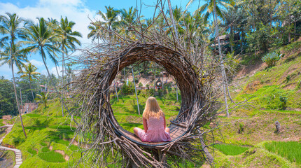 Blond girl is sitting on a large bird nest in the jungle near the rice terraces -  Bali island, Indonesia