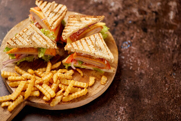 Chicken and cheese club sandwiches served on a wooden board with french fries
