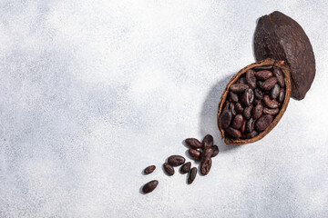 ЫSplit fermented cocoa pod with shelled cacao beans atop light grey backdrop, top view,  copy space