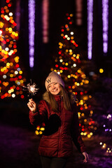 Christmas photography. the girl holds a sparkler in her hand, the lights of garlands on the tree are visible from behind