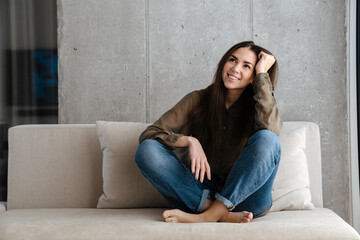 Happy brunette nice girl smiling while sitting on sofa at home