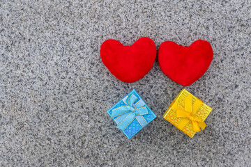 Two red hearts stand and two colored gift boxes lie on brown granite slab, valentine's day