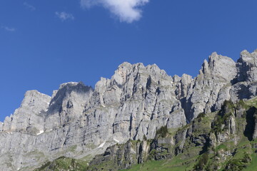 Majestically, steep rock faces of this sunlit mountain range rise high against a blue sky