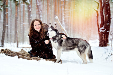 Portrait of a girl on a walk on a Sunny winter day with a Husky dog in the Park. The girl gently hugs the dog by the withers and looks at the camera. A man on white snow with a dog. People and dogs.
