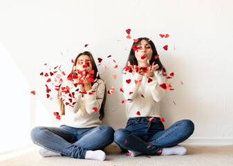 Two best friends having fun at home blowing red confetti