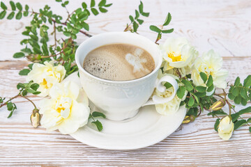 Summer coffee break concept in retro style. Vintage white cup of coffee and twig with white roses on white paint rustic wooden background