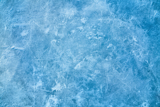 Ice blue background with ice skating tracks. Covered with a thin layer of snow. Rink. Frozen water, sea. Frosty ice texture with scratches in winter.
