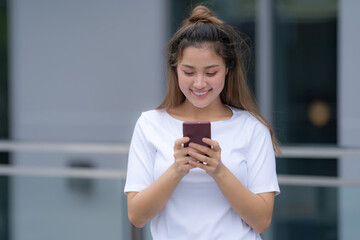 Woman in white t-shirt and blue jeans using phone standing on a floor outside in the city street background