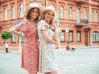 Naklejka premium Two young beautiful smiling hipster female in trendy summer sundress.Sexy carefree women posing on the street background in hats. Positive models having fun and hugging