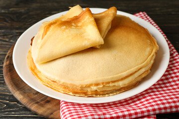 Board with thin pancakes on wooden background