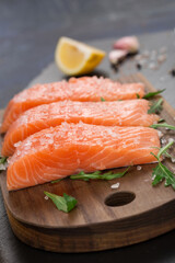 Raw fillet of salmon with sea salt, lemon and pepper on black stone background.