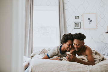 Obraz na płótnie Canvas Happy black couple playing on a smartphone in bed