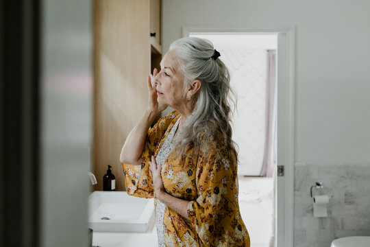 Elderly woman putting on a makeup in front of a mirror